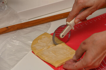 Woman slices soft dough into pieces for Parker House buns in a home kitchen.