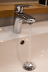 A sleek chrome faucet dispenses a steady stream of water into a pristine white sink, showcasing modern bathroom design with a minimalist aesthetic and clean lines