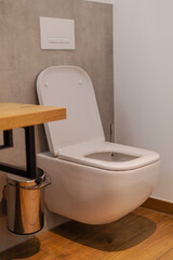 A sleek and modern toilet is positioned against a simple gray wall. Beside it, a wooden countertop provides a functional surface, while a metallic trash can completes the uncluttered look