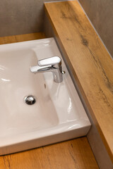 A minimalist basin features a polished chrome faucet, positioned on a warm wooden countertop, showcasing an elegant and contemporary bathroom aesthetic