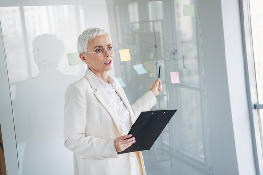 Businesswoman presenting at a meeting with a detailed whiteboard while wearing elegant formal attire in an office setting