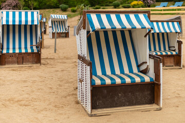 Blue and white striped beach chairs are arranged neatly on the sandy shore, creating a relaxing spot for visitors. The sun shines brightly, inviting leisure and enjoyment in this serene environment