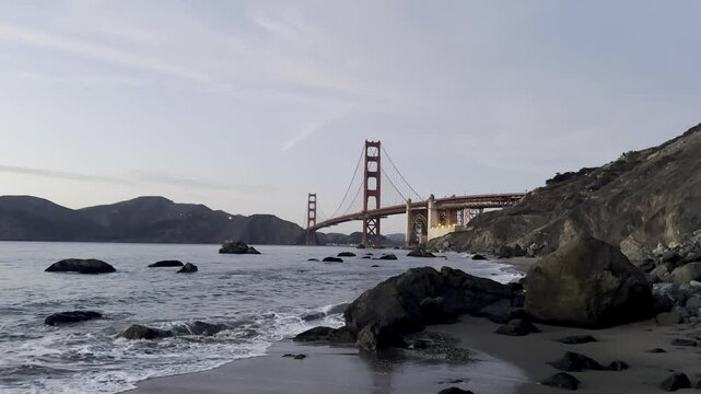 Waves crash at the beach in San Francisco, California with the Golden Gate Bridge in the background.