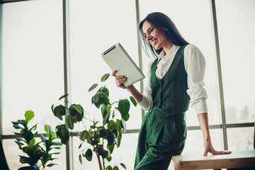 Confident businesswoman reading tablet in stylish office interior with greenery emphasizing...
