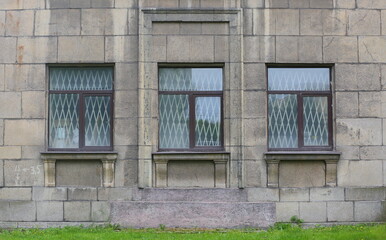 Three windows of an old house with bars inside