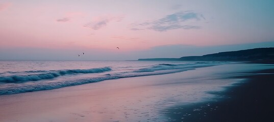 A tranquil beach at dusk with a soft pink sky and calm waves