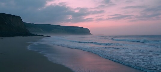 A tranquil beach at dusk with a soft pink sky and calm waves