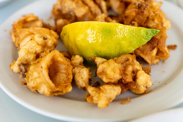 Golden fried calamari served on a white plate with a wedge of lemon, perfect as a seafood appetizer or snack.