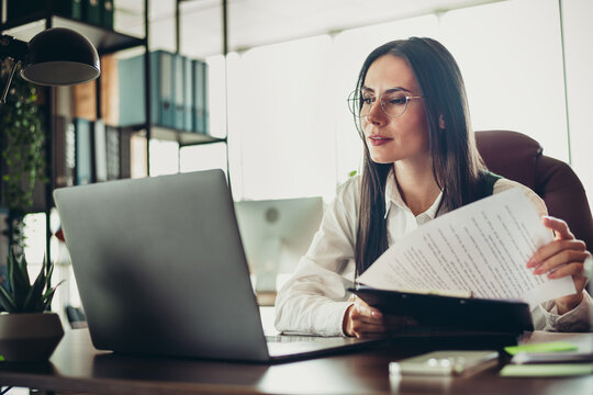 Fototapeta Professional businesswoman in formal attire working diligently at her office desk, reviewing documents and focusing on tasks.