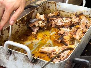 Juicy cooked pork in metal roasting pan with hand holding tongs