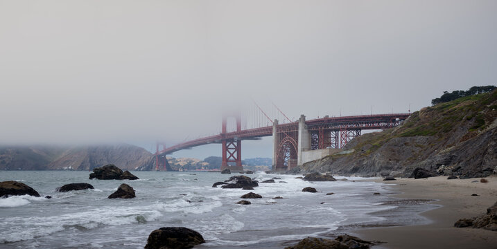 The Golden Gate Bridge in San Francisco, California disappears into the fog, as seen from the beach.