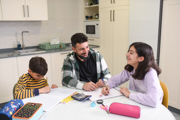 Father in the kitchen of his home helps his son and daughter with their homework on an autumn day