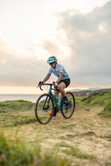 vertical Latin cyclist woman riding gravel bike by the sea at sunrise
