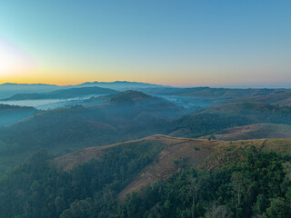 Aerial view of A breathtaking aerial view of a lush, green mountain range under a bright, clear blue sky, with sunlight illuminating the vast, rolling terrain and valleys below.