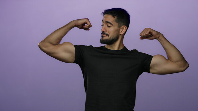Young man flexing muscles against isolated purple background displaying strength and confidence in a studio setting