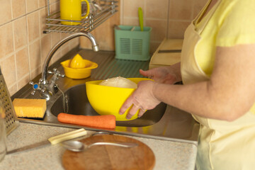Mature woman washing a whole cabbage head under running water in the kitchen — beginning the...