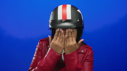Woman wearing helmet performing peekaboo in a background beside a young latin hispanic rider on a bike with motorbike style parts over a blue wall.