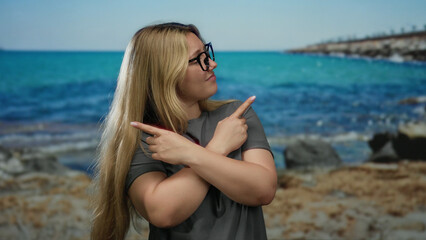 Woman posing with crossed arms pointing in different directions on a seaside with stunning blue sea and natural landscape in the background.