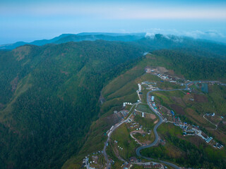 aerial view of a winding mountain road surrounded by lush greenery, scattered houses, and farmland. This scenic landscape captures the natural beauty and human settlement in a mountainous region.