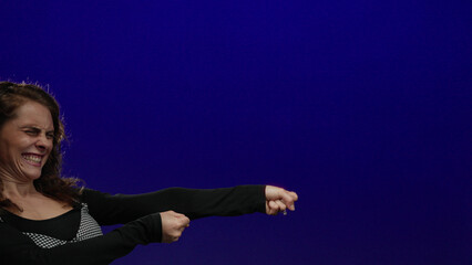 Young woman pulling on imaginary rope with determination against isolated blue background.