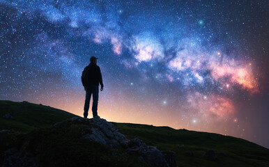 Glowing Milky Way and man on mountain trail at starry night. Silhouette of a guy on the hill, sky with bright stars. Galaxy. Space landscape with milky way. Nightscape. Travel background. Concept