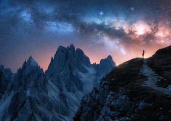 Glowing Milky Way and woman on mountain peak at starry night. Tre Cime, Dolomites, Italy. Galaxy. Space landscape with silhouette of a girl, trail, rocks, pink sky with stars. Milky Way and hiker