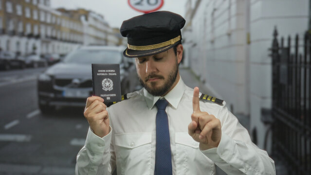 Fototapeta Young man in uniform stands outdoors on a street holding an italian passport, near a car in an urban setting under a speed sign.