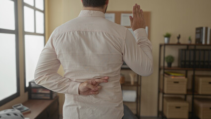 Young man in office making an oath with fingers crossed behind his back symbolizing deceit in a...