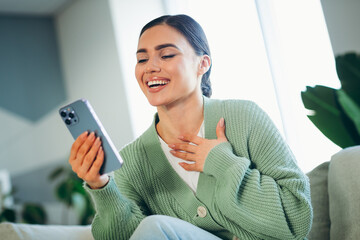 Young woman enjoying leisure time indoors, holding a phone while happily communicating, styled in...