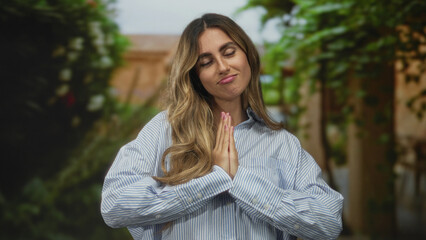 Obraz premium Woman presses palms together in a gentle pleading gesture in a sunlit garden surrounded by green vines; apology hope.