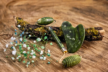 delicate cosmetic composition with gypsophila, quartz roller, gua sha on a mossy tree branch, on a...
