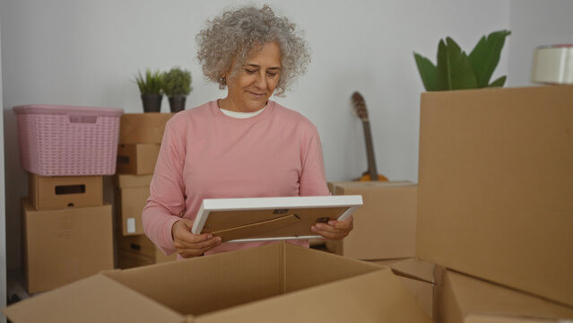 Woman unpacking a picture frame in a new home surrounded by cardboard boxes, reflecting a moment of nostalgia and new beginnings in a cozy indoor setting.