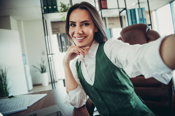 Obraz premium Charming businesswoman taking a selfie in a modern office environment showcasing professional success and empowerment