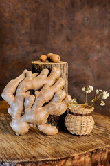 A close-up of fresh ginger root placed next to a small wicker basket with dried flowers, and three whole walnuts lying on a rough wooden log in the background. 