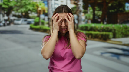Fototapeta premium Young woman with blonde hair appears stressed on a sunny urban street wearing a pink shirt and showcasing various expressions of frustration and confusion.