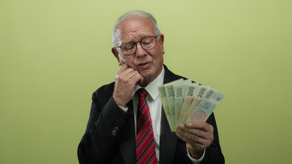 Senior man in business suit holding czech koruna banknotes thoughtfully over an isolated yellow...