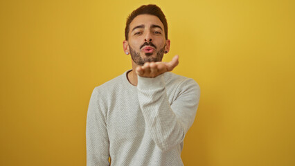 Obraz premium Young hispanic man blowing kiss isolated over bright yellow background showcasing emotion and connection through expressive gesture.