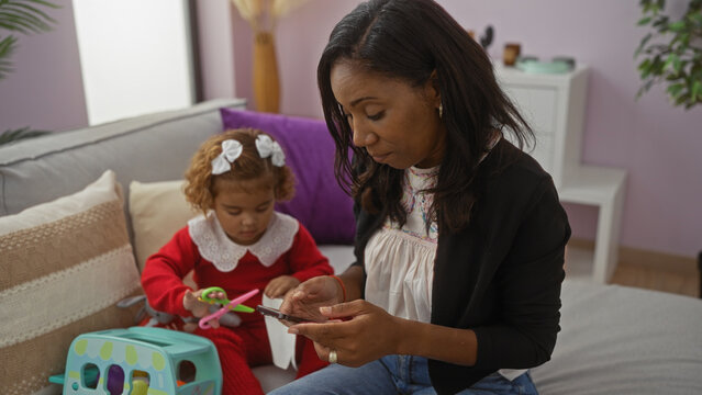 Woman and child sitting in living room, mother using smartphone while daughter plays with toy, cozy home atmosphere, showing family bond and love in a bright interior.