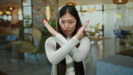 Woman gesturing stop with crossed arms indoors in a stylish hotel setting, showing clear expression and vibrant ambiance.