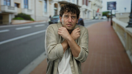 Obraz premium Man outdoors looking apprehensive on an empty street with buildings in the background.
