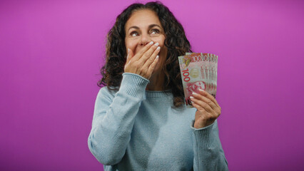 Middle-aged woman holding new zealand dollars on an isolated purple background, expressing surprise...