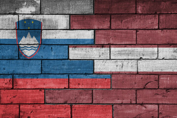 colourful painted big national flag of latvia and flag of slovenia on a massive old brick wall background. concept