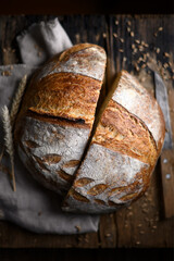 Rustic sourdough bread cutting in half with deep cracks and crisp skin on rustic wooden table. Hand-scored hearth loaf captured in natural ambient light