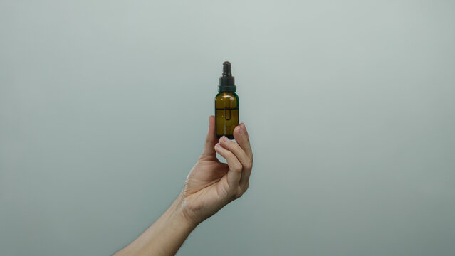 Caucasian man holding amber dropper bottle against isolated white wall background, showcasing hand detail and product clarity in minimalist setting.