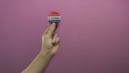 Caucasian man holds a voting badge against an isolated pink background, symbolizing civic...