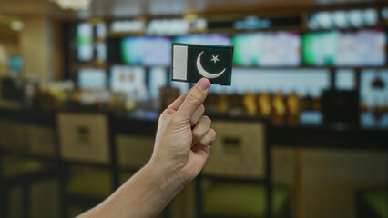 Man holding embroidered pakistan flag patch indoors in a coffee restaurant with a blurred background.