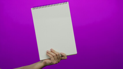 Obraz premium Man hand holding blank notebook against vibrant pink background offering empty space for creative text layout and design.