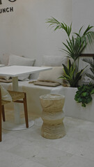 Modern restaurant interior featuring white table wooden stool green plants and beige cushions creating a cozy ambiance with natural decor and minimalist design.