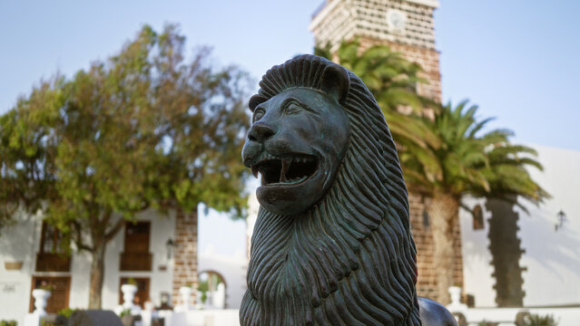 Lion statue in outdoor teguise lanzarote canary island daylight tree architecture church tower background travel