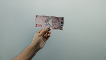 Man holding turkish lira banknote against a white wall background, showcasing financial concepts in...
